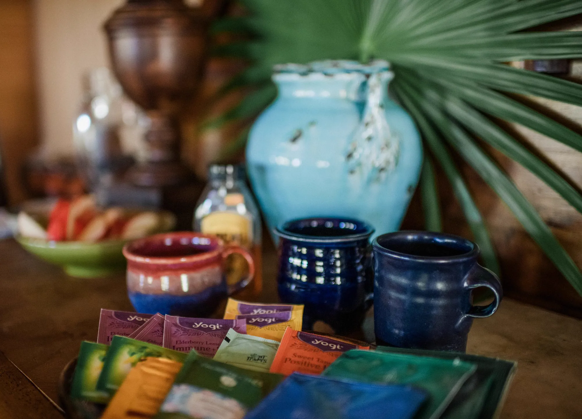 A tea station with mugs, a pitcher and an assortment of herbal teas.